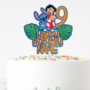 K&ouml;nnte beinhalten: Ein Tortenaufsatz mit den Figuren Lilo und Stitch, sowie der Zahl 9. Der Aufsatz hat einen blauen Glitzerumriss und den Text "Happy Birthday Name" in Orange. Der wei&szlig;e Kuchen ist mit bunten Streuseln verziert. Ideal f&uuml;r einen Geburtstag.