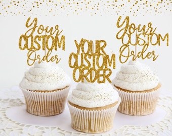 May include: Three gold glitter cupcake toppers with the text "Your Custom Order" on each. The toppers are on top of cupcakes with white frosting.