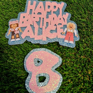 May include: Pink and blue glitter cake topper with the text "Happy Birthday Alice" and two cartoon figures. A separate pink and blue glitter number 8 cake topper.