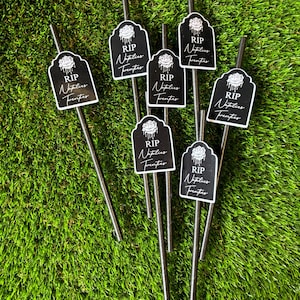 May include: Eight black straws with black and white paper flags attached. The flags have a white rose and the text "RIP Natalies Twenties".