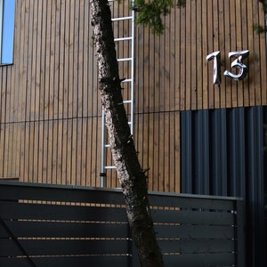 以下が含まれることがあります： 側面に梯子と金属製の数字「13」が付いた木造の建物。建物の前には濃い灰色のフェンスがある。