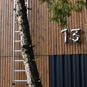 以下が含まれることがあります： 木造の建物に金属製の梯子が取り付けられています。建物の下部には黒い金属パネルがあり、木製のパネルには「13」の数字が表示されています。