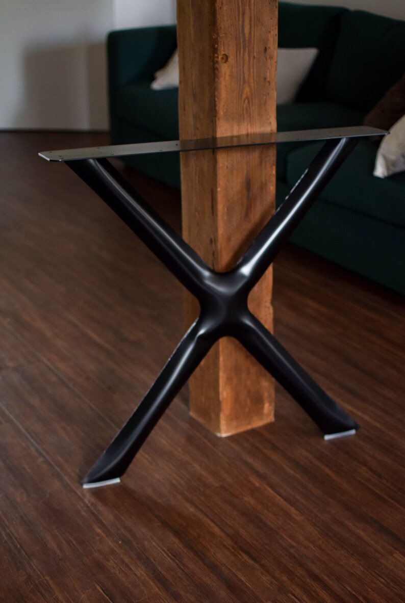 May include: Black metal table legs in an X shape, with a wooden post in the center. The legs are attached to the post with screws.
