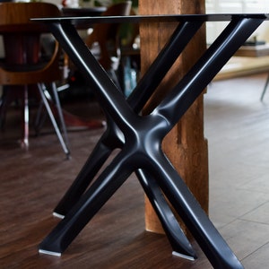May include: Black metal table legs with a criss-cross design. The legs are attached to a wooden beam.