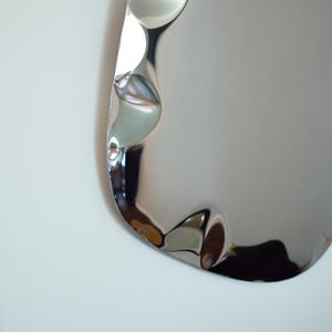May include: A close-up of a shiny, silver-colored, wavy-edged object. The surface reflects light, creating highlights and shadows. The object appears to be made of metal and has a smooth, polished finish. The overall shape is curved and organic.