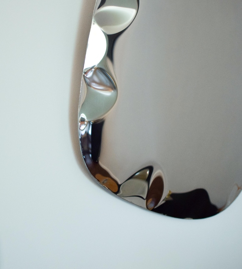May include: A close-up of a shiny, silver-colored, wavy-edged object. The surface reflects light, creating highlights and shadows. The object appears to be made of metal and has a smooth, polished finish. The overall shape is curved and organic.
