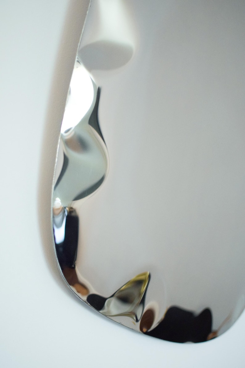 May include: A close-up of a shiny, silver-colored object with a unique, curved shape. The object has a reflective surface, with light and shadows creating interesting patterns. The design appears to be modern and abstract.