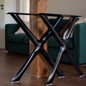 May include: Two black metal table legs with a criss-cross design. The legs are made of thick metal and have a smooth, black finish. The legs are attached to a wooden beam.