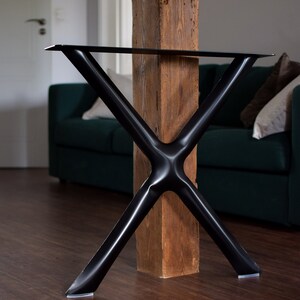 May include: Black metal table legs in an X shape with a wooden post in the center. The legs have rubber feet.