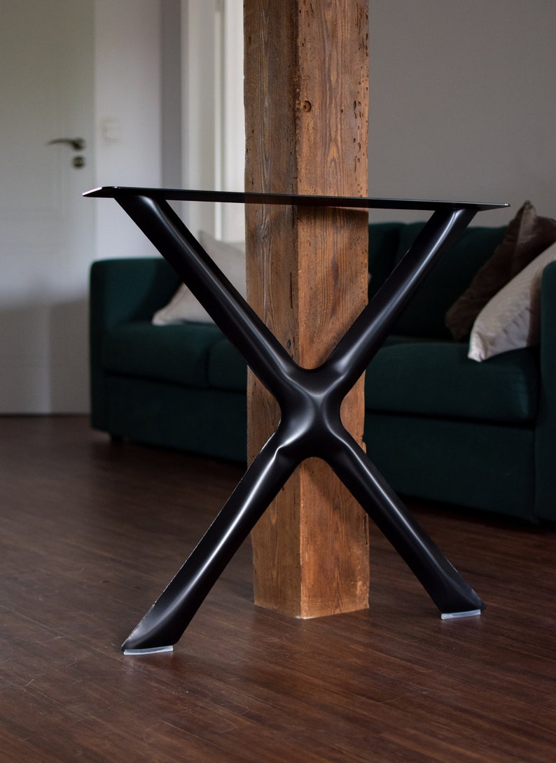 May include: Black metal table legs in an X shape with a wooden post in the center. The legs have rubber feet.