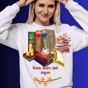 Peut inclure: Un sweat-shirt blanc à manches longues avec une impression graphique de livres empilés, de bougies, d'une tasse de café, d'une plume et d'un coussin doré. Le texte "Peace, books, and coffee" est imprimé en rouge avec des fleurs orange.