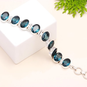Könnte beinhalten: Ein silbernes Armband mit einer Kette und ovalen blauen Topas-Edelsteinen.
