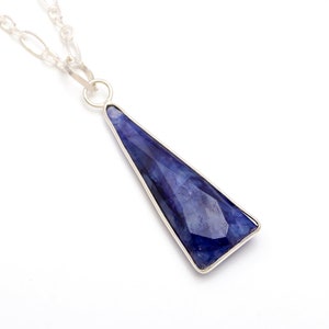 Puede incluir: Un collar de cadena de plata con un colgante que presenta una gran piedra preciosa azul facetada engastada en un marco de plata.