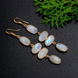 Pode incluir: Um par de brincos de ouro com várias pedras de lua ovaladas. Os brincos têm um design delicado e feminino.