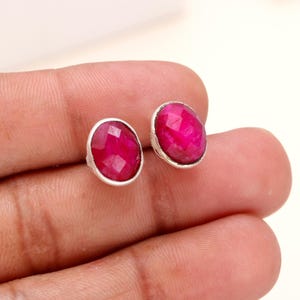 Könnte beinhalten: Ein Paar silberne Ohrstecker mit rosafarbenen Rubinen. Die Ohrringe sind rund und haben eine glatte, polierte Oberfläche.
