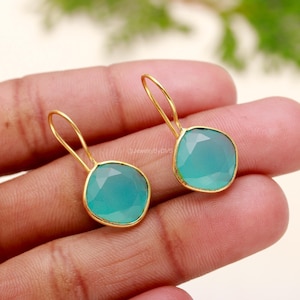 Peut inclure: Une paire de boucles d'oreilles pendantes en or avec des gouttes de pierres précieuses bleu clair. Les boucles d'oreilles ont un design simple et sont parfaites pour tous les jours.