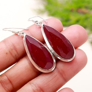 May include: A pair of teardrop-shaped earrings with faceted, deep red gemstones set in silver-colored metal. The earrings have a simple hook design for pierced ears, showcasing the vibrant color of the stones.