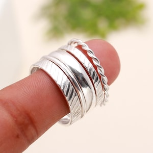 May include: A set of four silver stacking rings. The rings are all different widths and have a variety of textures, including smooth, textured, and braided.