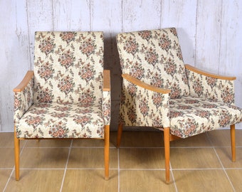 May include: Two floral patterned armchairs with wooden frames and legs. The chairs have a light beige background with a floral pattern in shades of pink, brown, and green.