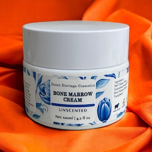 Op de afbeelding: Een witte pot met een blauw-wit bloemenmotief. De pot bevat beenmergcrème, die ongeparfumeerd is. De pot is gelabeld met "Dutch Heritage Cosmetics" en "Net 120ml | 4.2 fl oz".