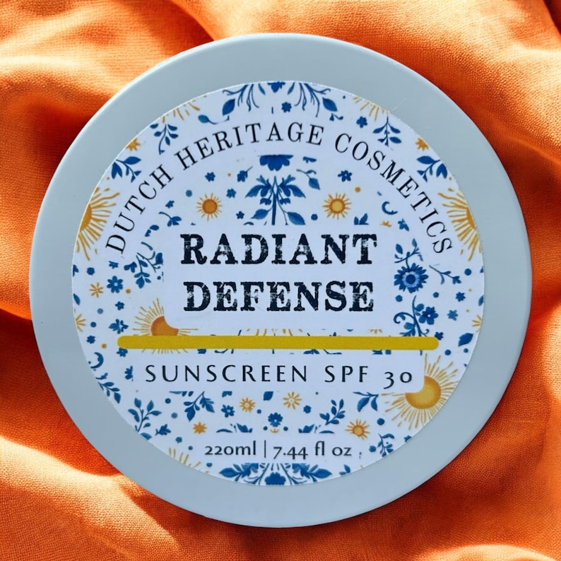 Op de afbeelding: Een ronde, lichtblauwe container van Dutch Heritage Cosmetics Radiant Defense Sunscreen SPF 30. Het etiket heeft een bloemenontwerp met blauwe en gele accenten, en de tekst "220ml | 7.44 fl oz."