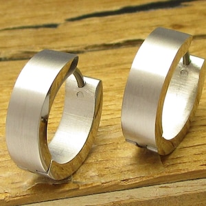 May include: A pair of silver hoop earrings with a brushed finish. The earrings are made of metal and have a simple, modern design.