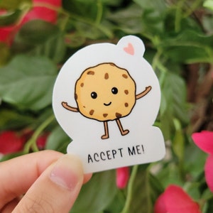 May include: A white sticker with a cartoon chocolate chip cookie with arms and legs. The cookie is smiling and has a heart above its head. The text "ACCEPT ME!" is below the cookie.