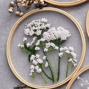 May include: White embroidered flowers in a wooden embroidery hoop. The flowers are delicate and have a natural, rustic look.