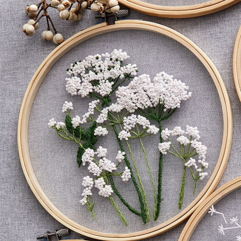 May include: White embroidered flowers in a wooden embroidery hoop. The flowers are delicate and have a natural, rustic look.