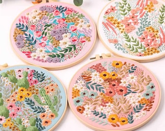 May include: Four embroidery hoops featuring floral designs. The hoops are made of wood and have pink, blue and white fabric stretched over them. The designs are all different and feature various flowers, leaves and other botanical elements.