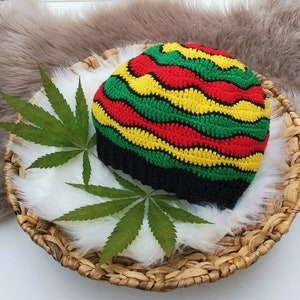 May include: A crocheted hat with red, yellow and green stripes. The hat is on a woven basket with a white fluffy surface and a green leaf.
