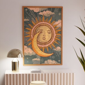 May include: A framed print of a vintage illustration of the sun and moon. The sun has a human face and the moon is a crescent shape. The background is a blue and green sky with clouds and stars.