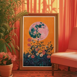 May include: A framed print of a pink and green moon with a field of flowers in the foreground. The moon is set against an orange background. The print is framed in a gold frame.