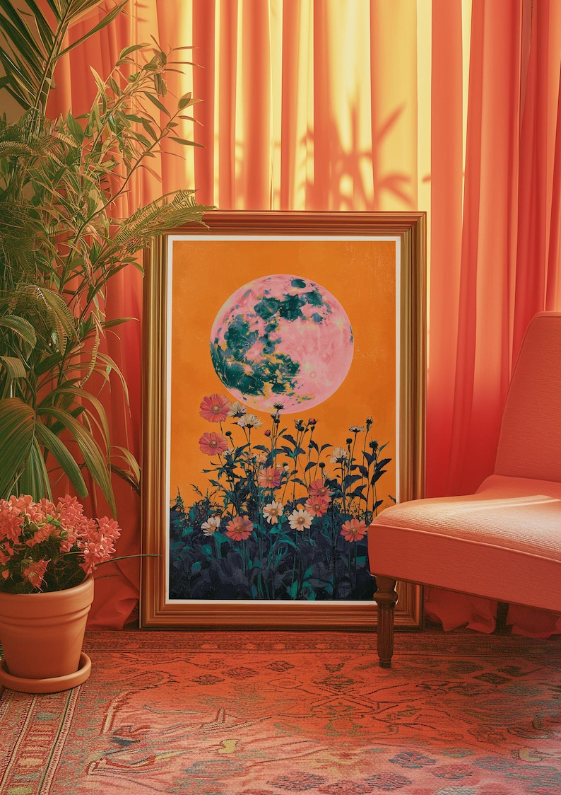 May include: A framed print of a pink and green moon with a field of flowers in the foreground. The moon is set against an orange background. The print is framed in a gold frame.