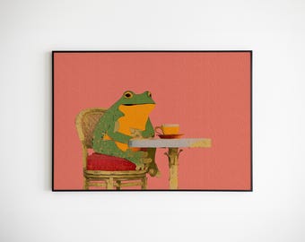 May include: A framed art print featuring a green and orange frog seated at a small table with a teacup. The frog is sitting on a wicker chair with a red cushion. The background is a solid coral color.