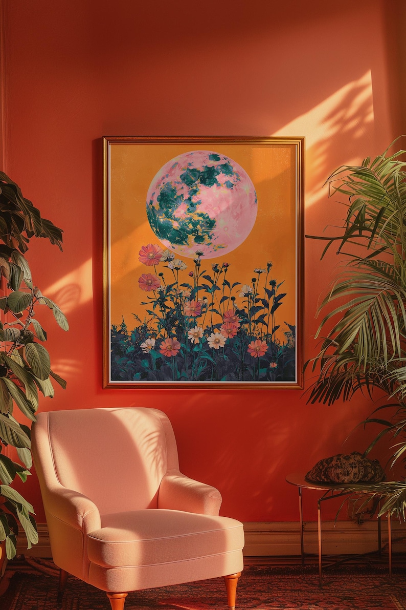 May include: A framed print of a pink and green moon with a field of flowers in front of it. The print is hanging on an orange wall.