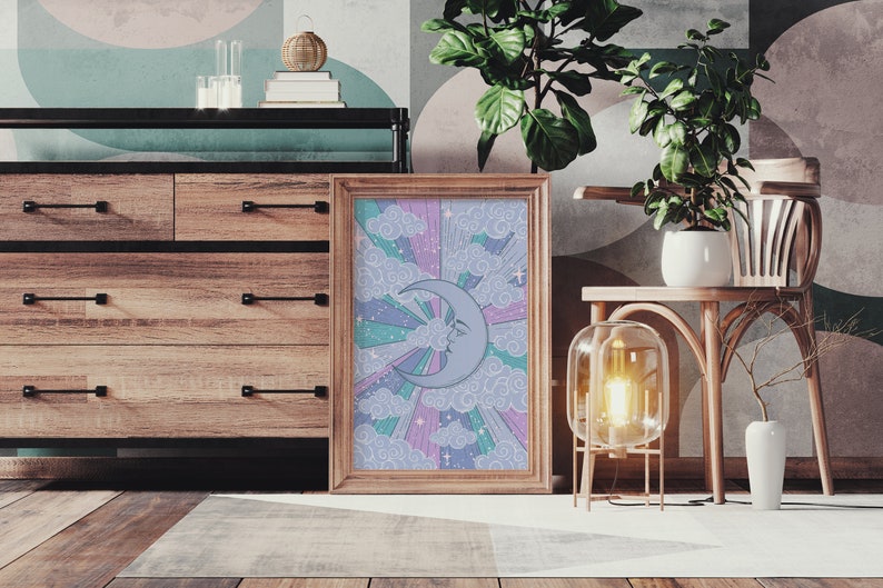 May include: A framed print of a crescent moon with a face, surrounded by clouds and rainbow-colored rays. The print is in a wooden frame and is hanging on a wall.