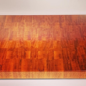 Op de afbeelding: Een rechthoekig aanrechtblad van slagersblokken gemaakt van verschillende stukken hout. Het hout heeft een warme, roodbruine tint met variaties in toon. Het oppervlak is glad en lijkt verzegeld te zijn, waardoor het licht reflecteert. Geschikt voor gebruik in de keuken.