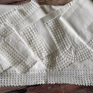 K&ouml;nnte beinhalten: Ein wei&szlig;es Leinentischtuch und passende Servietten mit aufwendiger H&auml;kelspitze. Das Set liegt auf einer Holzoberfl&auml;che und zeigt die filigrane Handwerkskunst und das klassische Design.