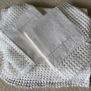 K&ouml;nnte beinhalten: Ein gefaltetes wei&szlig;es Leinen-Bettw&auml;sche-Set mit aufwendiger H&auml;kelspitze. Das Set enth&auml;lt Kissenbez&uuml;ge und ein Laken, alles in einer neutralen Farbe. Die Spitzendetails verleihen der Bettw&auml;sche eine Vintage- und handwerkliche &Auml;sthetik.