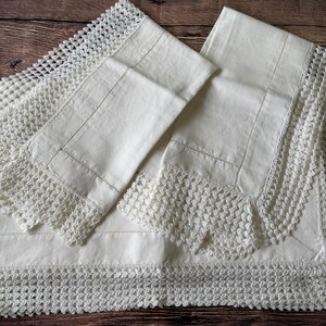 K&ouml;nnte beinhalten: Cremefarbene Bettw&auml;sche mit aufwendiger H&auml;kelspitze. Das Set beinhaltet ein Bettlaken und zwei Kissenbez&uuml;ge, alle ordentlich gefaltet. Die H&auml;kelarbeit verleiht der Bettw&auml;sche eine zarte, vintage &Auml;sthetik.