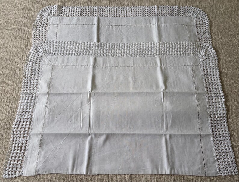 K&ouml;nnte beinhalten: Zwei wei&szlig;e, rechteckige Kissenbez&uuml;ge mit geh&auml;keltem Rand. Die Kissenbez&uuml;ge sind aus einem glatten, hellen Stoff gefertigt und haben ein schlichtes, elegantes Design. Der geh&auml;kelte Rand sorgt f&uuml;r eine besondere Textur und Detail.