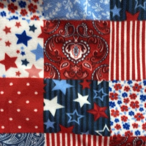 May include: A fleece fabric featuring a patchwork design with alternating squares of red, white, and blue patterns. The motifs include stars, stripes, floral prints, paisley swirls, and polka dots. A white measuring tape is visible at the bottom edge.