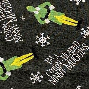 May include: Dark grey fabric featuring a repeating pattern of green elf illustrations, white snowflakes, and the text "I'M A COTTON-HEADED NINNY MUGGINS". The elves have green tops and yellow trousers.