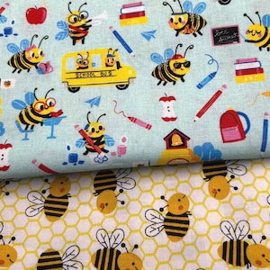 Op de afbeelding: Twee stukken stof met een bijen thema. De bovenste stof is lichtblauw met een gele schoolbus, rode appels, potloden en bijen. De onderste stof is wit met een geel honingraatpatroon en bijen.
