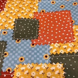 May include: A patchwork fabric with a variety of floral patterns in shades of yellow, orange, red, blue, and green. The fabric is made up of squares and rectangles, each with a different pattern.