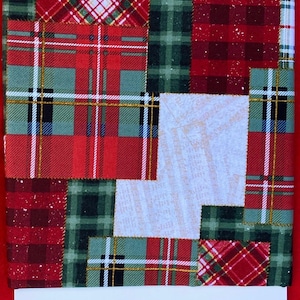 May include: A patchwork fabric with a red, green, and white plaid pattern. The fabric is made up of different squares of plaid, each with a different color combination. The fabric is perfect for quilting, sewing, or crafting.