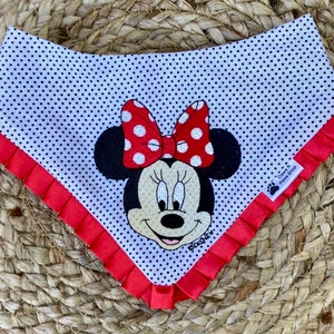 May include: White dog bandana with red polka dots and a red frilled trim. The bandana features an embroidered image of Minnie Mouse with a red bow and white polka dots. The text "DISNEY" is embroidered below Minnie Mouse. The text "Claws N Paws Shop" is printed on a white tag attached to the bandana.