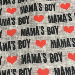 May include: A gray fabric with a repeating pattern of the text "Mama's Boy" in black and red hearts.