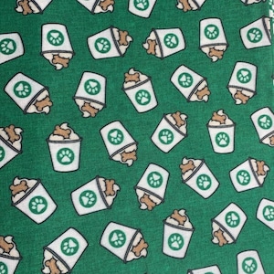 May include: Green fabric with a repeating pattern of white cups filled with brown swirls and a paw print on the side.